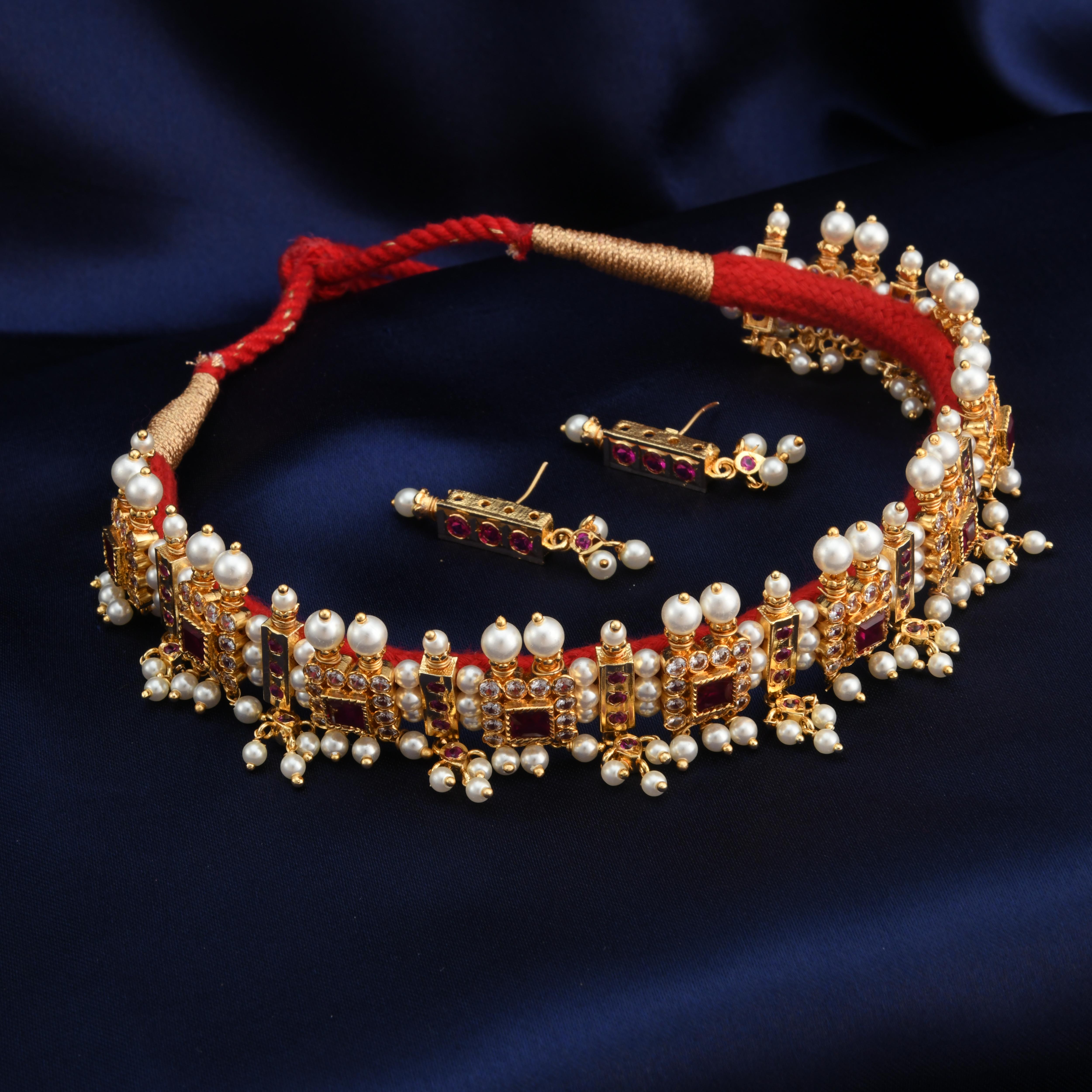 A Maharashtrian Chinchpeti necklace with gold, pink, and red colors, featuring pearl-like beads and red embellishments.